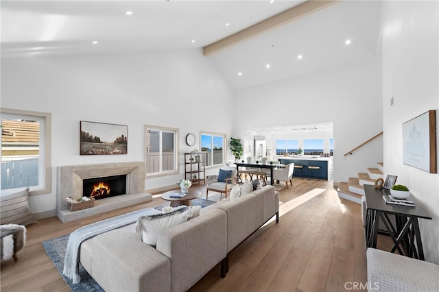 living room with beamed ceiling, high vaulted ceiling, a high end fireplace, and light hardwood / wood-style floors