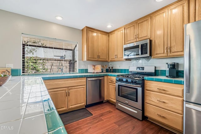 kitchen with dark wood-type flooring, sink, tile countertops, stainless steel appliances, and decorative backsplash