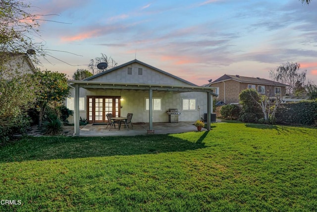 back house at dusk featuring cooling unit, a yard, a patio area, and french doors