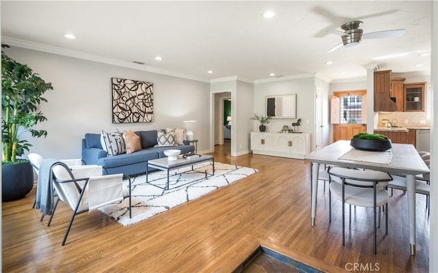 living room with wood-type flooring, ornamental molding, sink, and ceiling fan