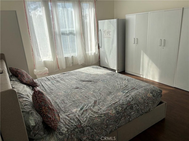 bedroom with multiple windows, dark wood-type flooring, and refrigerator