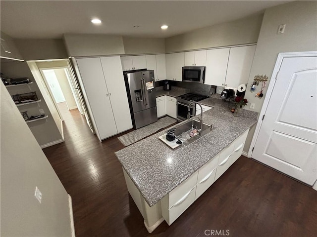 kitchen with sink, white cabinetry, stainless steel appliances, dark hardwood / wood-style flooring, and kitchen peninsula