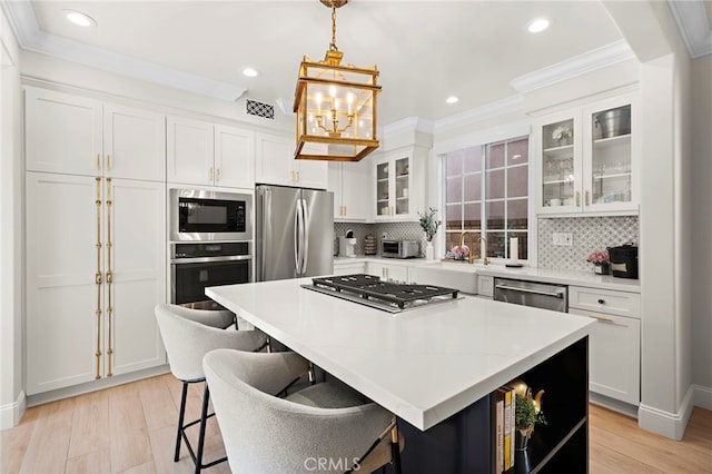 kitchen with a kitchen island, appliances with stainless steel finishes, decorative light fixtures, white cabinetry, and a kitchen bar