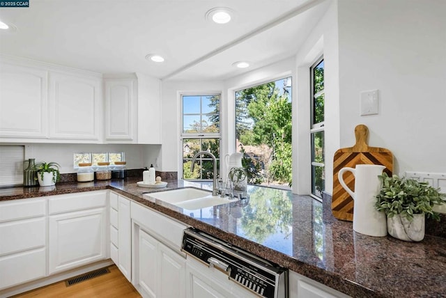 kitchen with white cabinetry, dishwasher, sink, dark stone counters, and light wood-type flooring