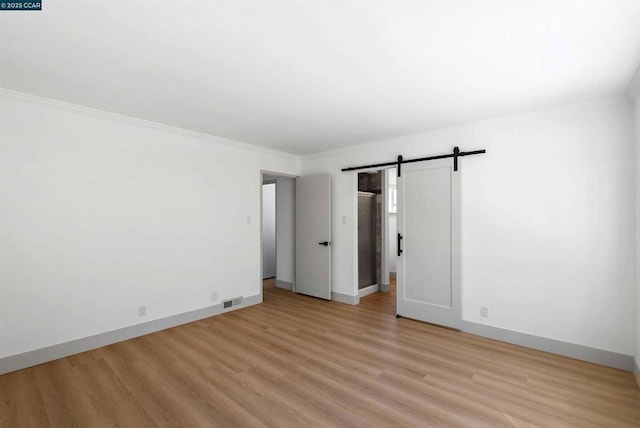 spare room featuring ornamental molding, a barn door, and light hardwood / wood-style flooring