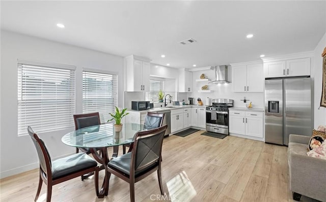 kitchen featuring appliances with stainless steel finishes, white cabinets, light hardwood / wood-style floors, and wall chimney exhaust hood