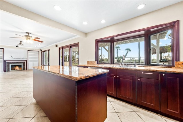 kitchen featuring light tile patterned floors, ornamental molding, a kitchen island, ceiling fan, and light stone countertops