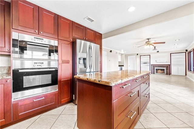 kitchen featuring light stone counters, light tile patterned floors, appliances with stainless steel finishes, a kitchen island, and ceiling fan