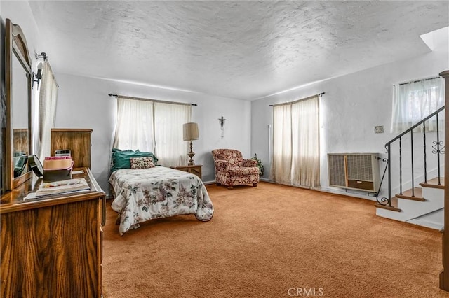 carpeted bedroom with heating unit, multiple windows, and a textured ceiling