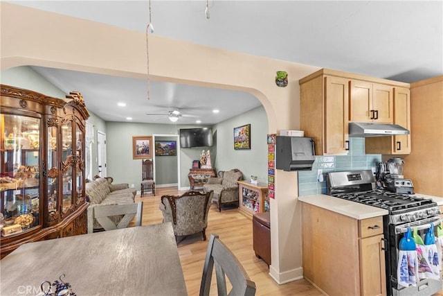 kitchen featuring stainless steel gas stove, open floor plan, light countertops, light brown cabinetry, and under cabinet range hood