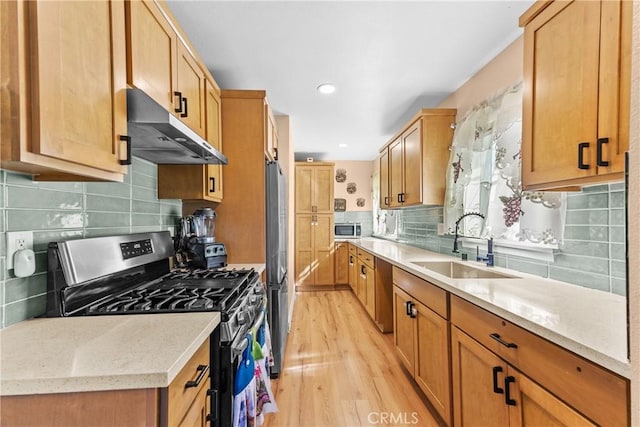 kitchen with under cabinet range hood, stainless steel appliances, a sink, light wood-type flooring, and backsplash