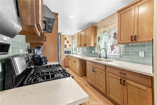 kitchen with light stone counters, light wood finished floors, backsplash, appliances with stainless steel finishes, and a sink