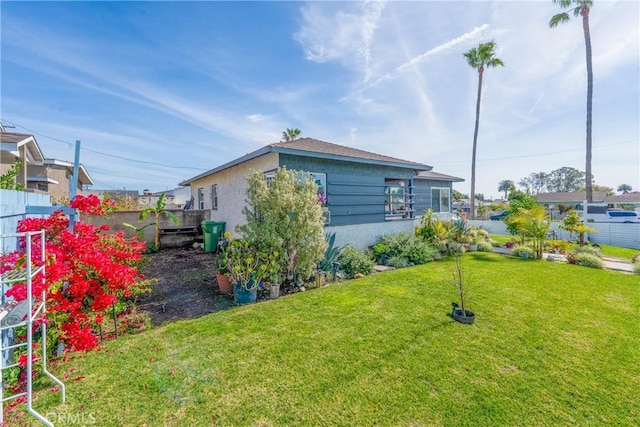 view of side of home featuring stucco siding, a lawn, and fence