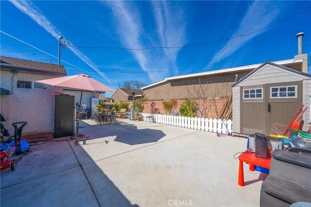 view of patio featuring fence, a storage unit, outdoor dining area, and an outbuilding