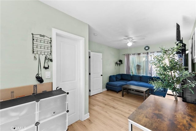 living room featuring light wood-style flooring, baseboards, and a ceiling fan