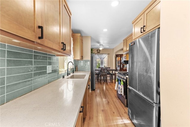 kitchen featuring sink, decorative backsplash, ceiling fan, stainless steel appliances, and light wood-type flooring