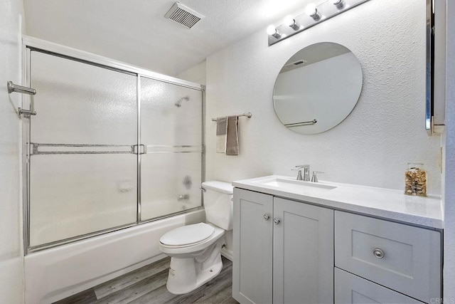 full bathroom featuring wood-type flooring, combined bath / shower with glass door, vanity, and toilet