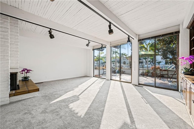 unfurnished living room with rail lighting, beam ceiling, floor to ceiling windows, a brick fireplace, and light colored carpet