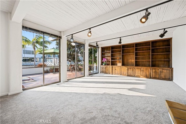 unfurnished living room featuring expansive windows, built in features, rail lighting, and light carpet