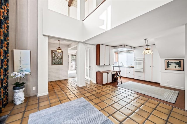 kitchen featuring white cabinetry, sink, hanging light fixtures, a high ceiling, and tile patterned flooring