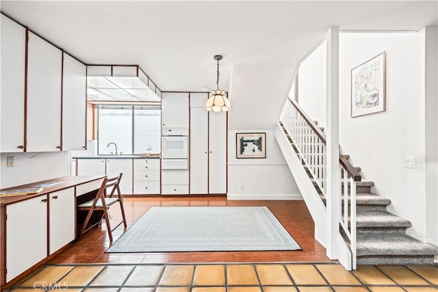 kitchen with white cabinetry, hanging light fixtures, sink, and white oven