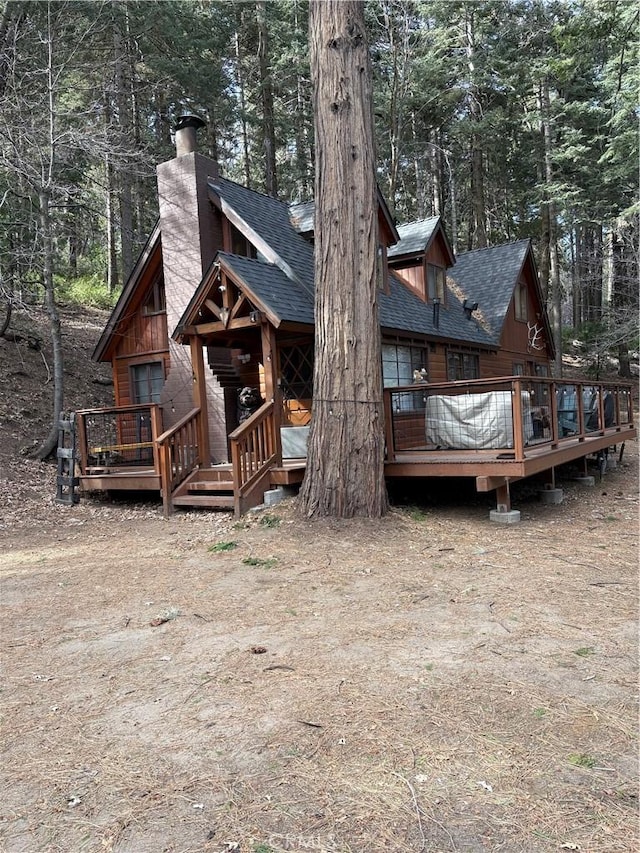 back of house featuring a wooden deck, a chimney, and roof with shingles