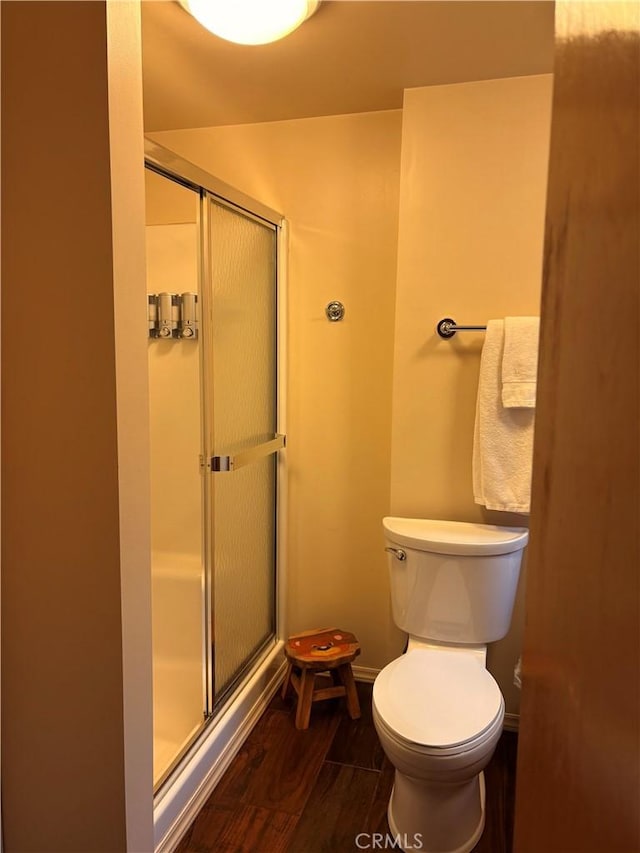 full bathroom featuring toilet, wood finished floors, a stall shower, and baseboards