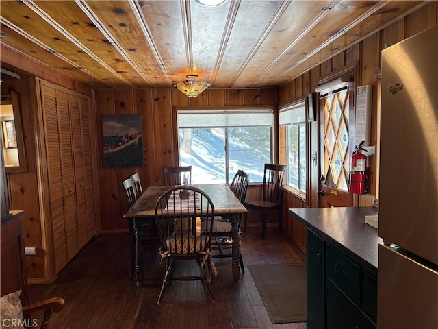 dining room featuring dark wood finished floors, wooden ceiling, and wooden walls