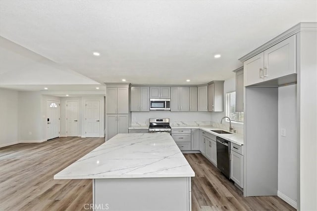 kitchen featuring sink, gray cabinetry, stainless steel appliances, light stone counters, and a kitchen island