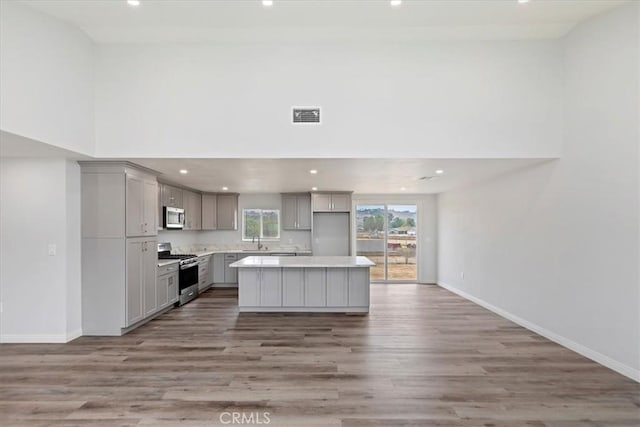 kitchen with gray cabinets, a kitchen island, appliances with stainless steel finishes, sink, and hardwood / wood-style flooring