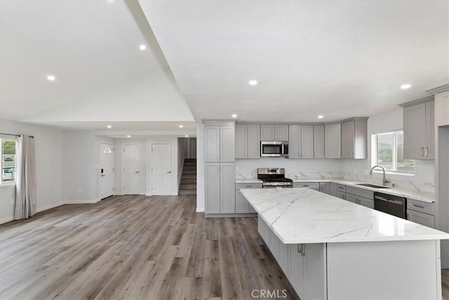 kitchen with gray cabinets, a kitchen island, sink, light stone counters, and stainless steel appliances