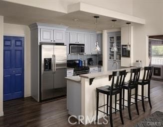 kitchen featuring dark wood-type flooring, a breakfast bar area, appliances with stainless steel finishes, white cabinetry, and hanging light fixtures