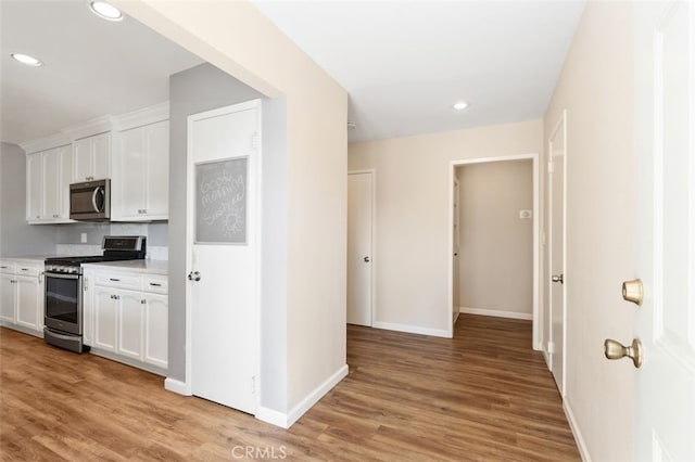 kitchen with appliances with stainless steel finishes, white cabinets, and light hardwood / wood-style flooring