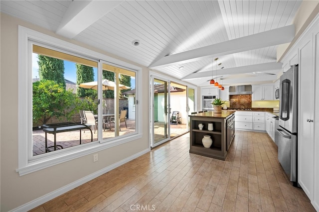 kitchen featuring decorative light fixtures, vaulted ceiling with beams, stainless steel fridge, white cabinets, and a center island