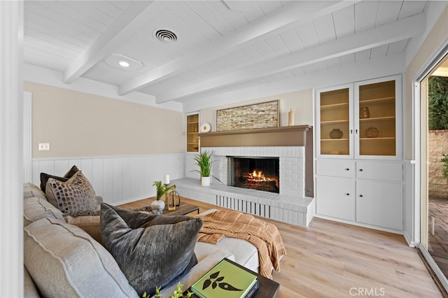 living room featuring beam ceiling, wood ceiling, a brick fireplace, light wood-type flooring, and built in shelves