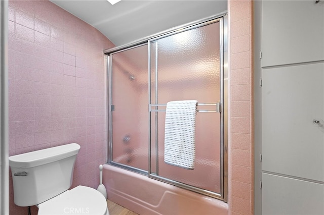 bathroom with toilet, combined bath / shower with glass door, and tile walls