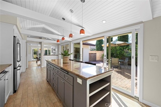 kitchen with a wealth of natural light, beamed ceiling, dark stone countertops, hanging light fixtures, and a center island