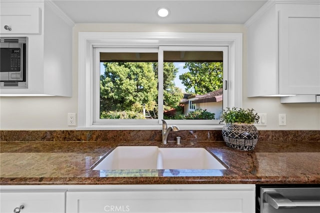 kitchen featuring white cabinetry, sink, stainless steel microwave, and dark stone counters