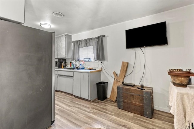 kitchen with stainless steel refrigerator, gray cabinets, sink, and light wood-type flooring