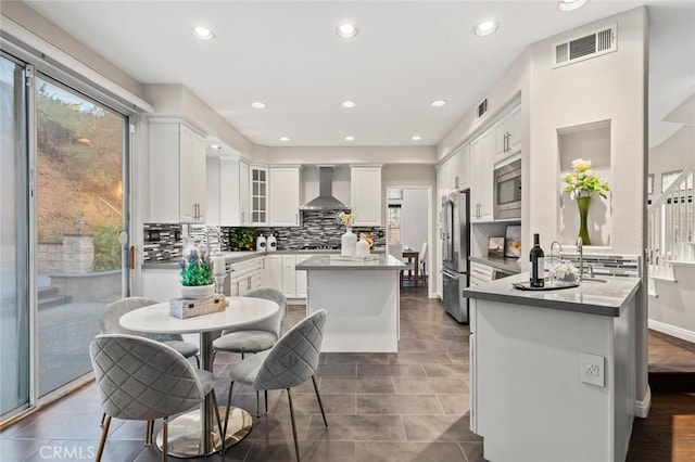 kitchen featuring wall chimney exhaust hood, tasteful backsplash, appliances with stainless steel finishes, a kitchen island, and white cabinets