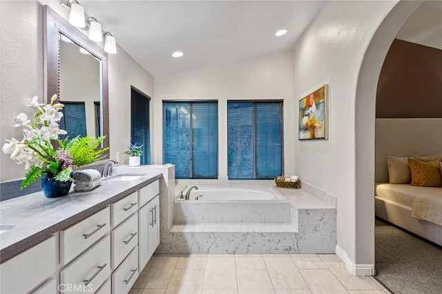 bathroom with vanity, tiled tub, vaulted ceiling, and tile patterned floors