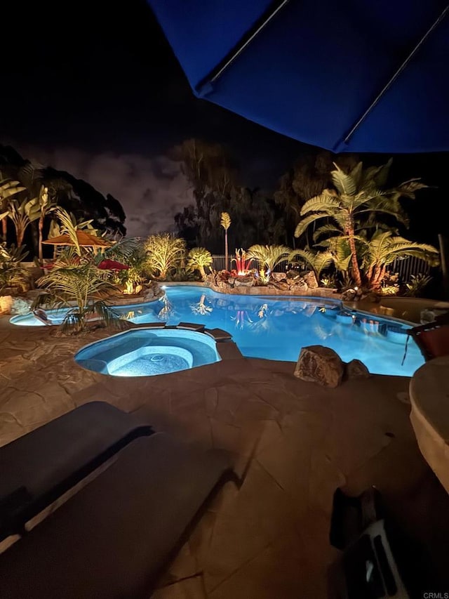 pool at twilight featuring an in ground hot tub