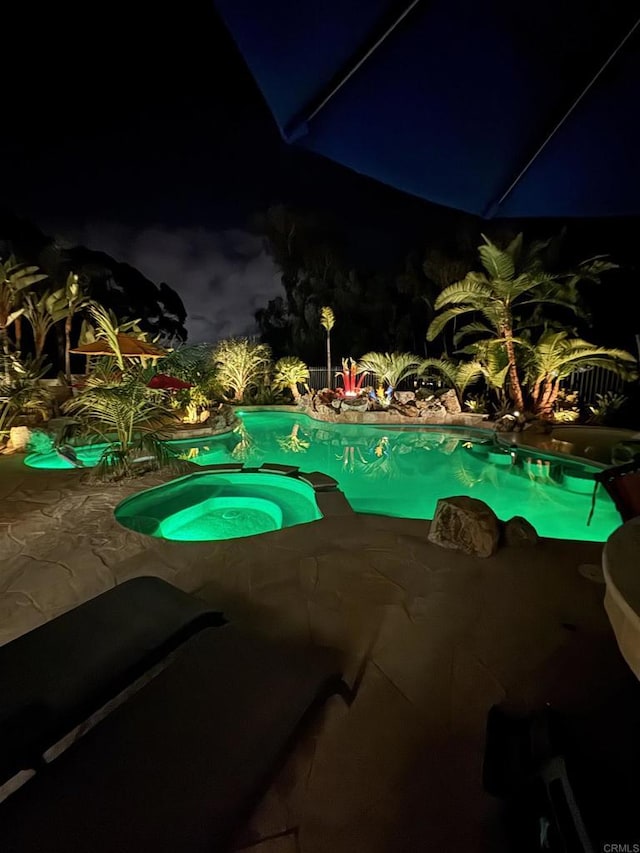 pool at night featuring an in ground hot tub