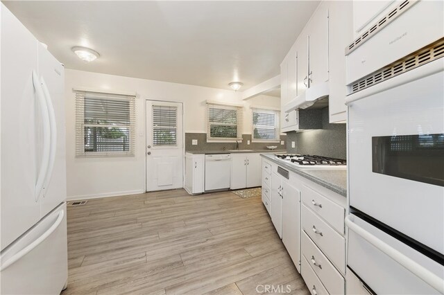 kitchen with sink, white appliances, light hardwood / wood-style flooring, white cabinetry, and backsplash