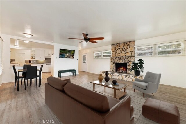 living room with ceiling fan, a stone fireplace, and light hardwood / wood-style flooring