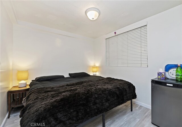 bedroom with stainless steel fridge and light hardwood / wood-style flooring