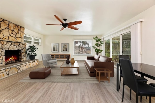 living room featuring a fireplace, ceiling fan, and light wood-type flooring