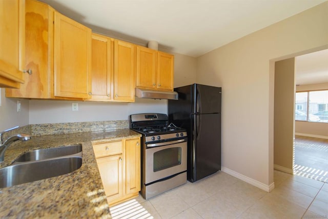 kitchen with sink, stainless steel gas range, light stone counters, black fridge, and light brown cabinetry