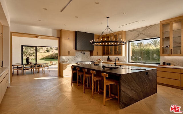 kitchen with sink, backsplash, light parquet floors, a kitchen island with sink, and an inviting chandelier