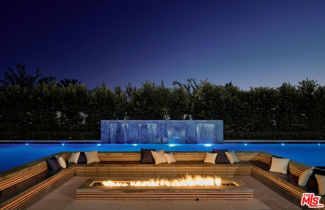 pool at night featuring pool water feature, a patio area, and an outdoor fire pit